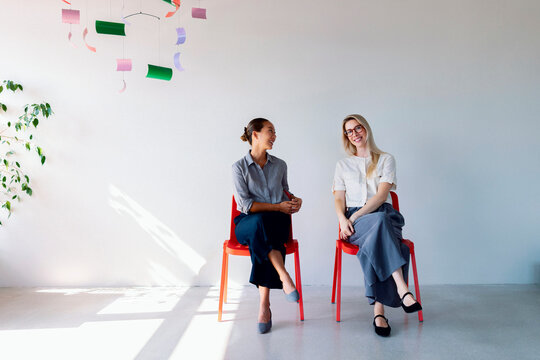 Two Women Sitting on Red Chairs Having a Friendly Conversation