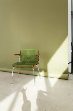Simple green chair with wooden armrests against an olive backdrop