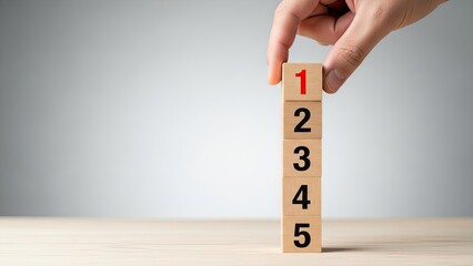 Hand placing number 1 block on top of stacked numbered wooden blocks concept