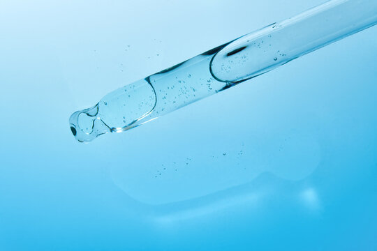 Glass pipette with liquid on gradient blue backdrop. 