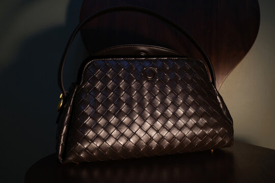 Elegant dark woven handbag displayed on a wooden chair
