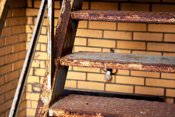Old rusted metal staircase leaning against weathered brick structure with warm lighting