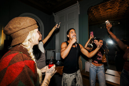 Diverse friends enjoying karaoke party, singing and filming