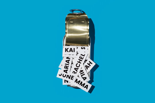 a shiny tin can filled with printed baby names on a vivid blue surface