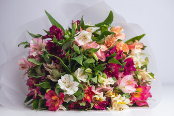 Bright bouquet of multicolored buds on a white table with a white background. Alstroemeria flowers in matte packaging. Floral background for a spring card for Mother's Day or March 8th, flower shop