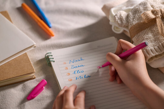 A person is writing a list of names on a notepad with a pink pen.