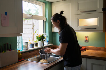 Young Man Handwashing Dishes in a Bright Kitchen During Daytime