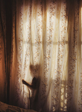 Child playing behind sheer floral curtains
