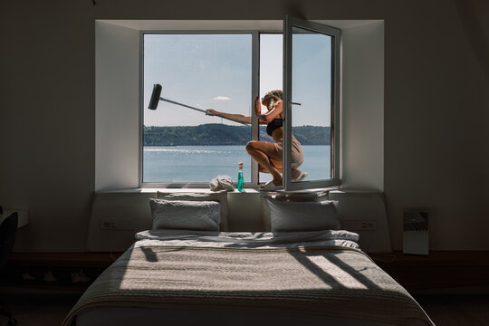 Woman Cleaning Window With a Squeegee in a Modern Bedroom