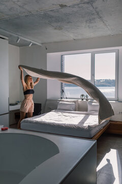 Woman Making Bed in Bright Minimalist Bedroom with Lake View