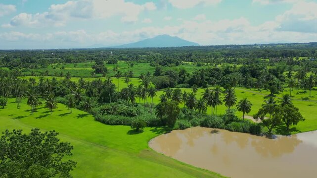 A forward aerial gliding over the fairways and ponds of Canlubang Golf and Country Club, gradually revealing lush greenery and a distant mountain backdrop in Calamba Laguna, Philippines