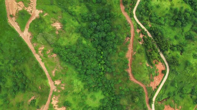 A rotating top view aerial revealing winding dirt roads cutting through green hills and patches of exposed soil of the natural terrain in Quinawan mountain view, Mariveles Bataan, Philippines