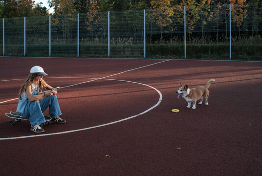 Girl playing with a corgi dog at a park during sunset
