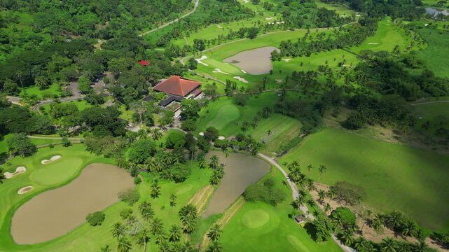 A downward aerial showing the clubhouse, fairways, water features, and tropical trees with drifting clouds casting soft shadows in Calamba Laguna, Philippines