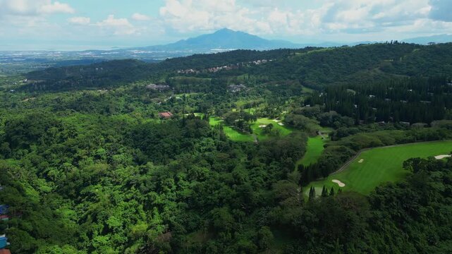 A higher forward aerial of Canlubang Golf and Country Club with tropical trees, fairways, cloud shadows, and distant Mount Makiling in Calamba Laguna, Philippines