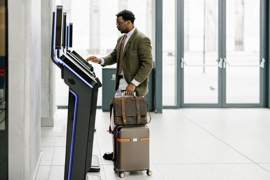 Traveler Checks in at Airport Kiosk With Luggage During Daytime