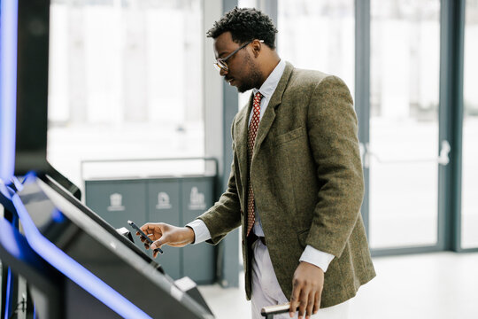 Businessman Using Mobile Device for Digital Access on Ticket Machine
