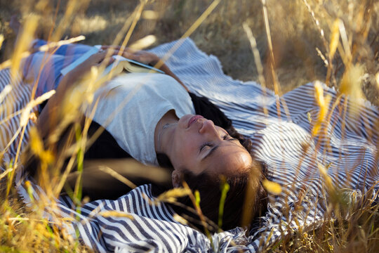 Relaxed woman resting in a field on striped blanket, peaceful mo