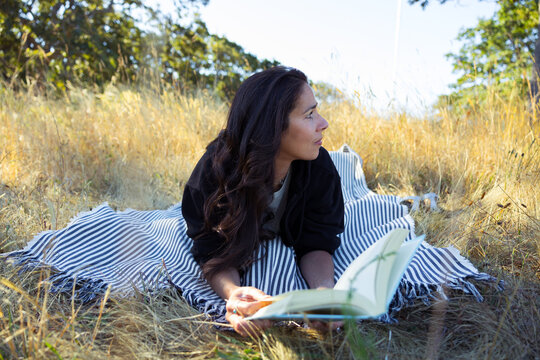 Woman reading outdoors on a striped blanket in a sunlit field