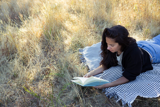Candid outdoor reading moment: woman lying on blanket reading bo