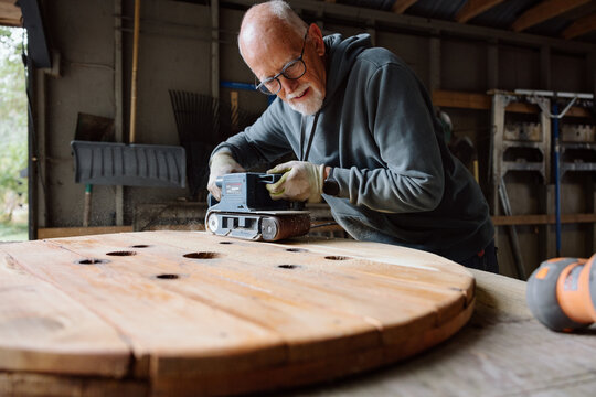 Candid woodworker sanding a large circular table in a workshop