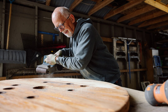 Candid moment: elderly man grinding wood in a busy workshop, smiling
