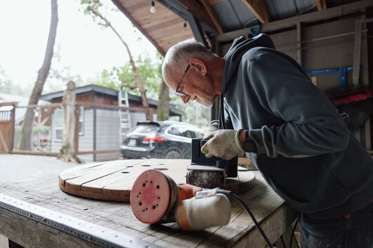 Candid elderly craftsman polishing a wooden disk in a workshop