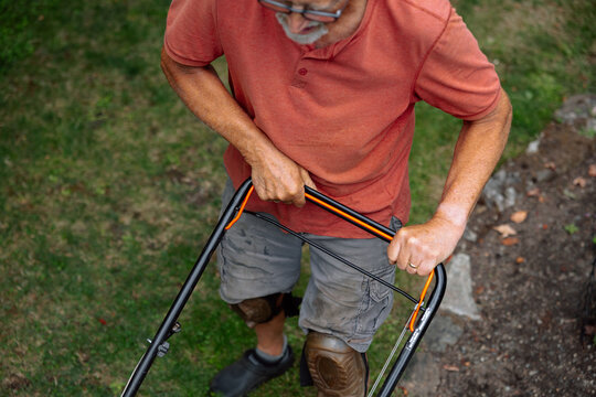 Candid moment of an older man mowing the lawn with a manual mower