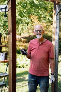 Candid outdoor portrait of a smiling older man staining in backyard