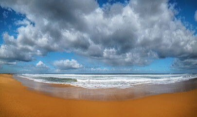 Beach panorama with incoming waves beneath dramatic cloudy sky
