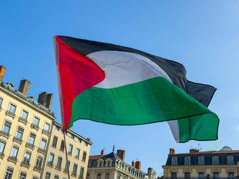 Palestinian Flag Waving in a Clear Blue Sky Over City Buildings