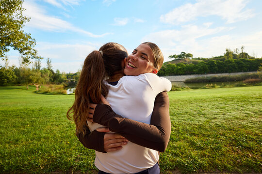 Two friends embrace joyfully in a park during a sunny day