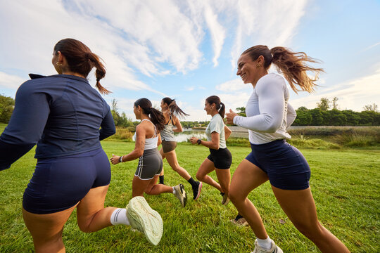 Women running on a grassy path by a lake in the afternoon sun