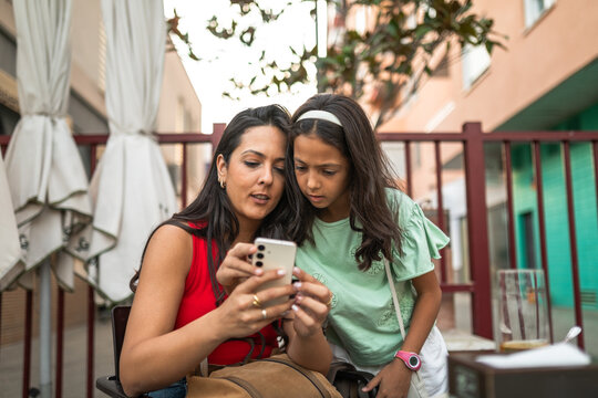 Mother and daughter using smartphone at outdoor café