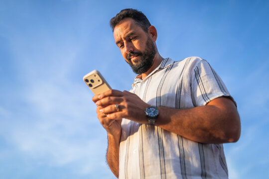 Bearded man using smartphone with blue sky background