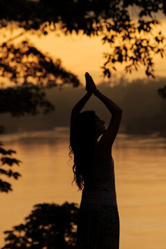 Silhouette of woman meditating in tropical rainforest at sunrise