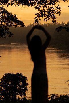 Silhouette of woman meditating in tropical rainforest at sunrise