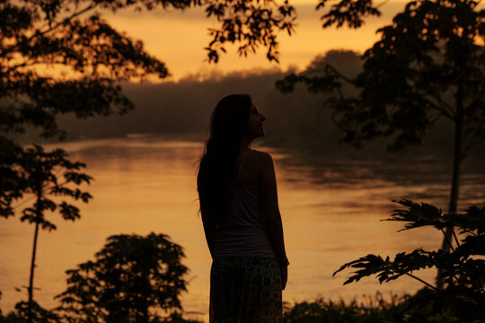 Silhouette of woman by river at tropical rainforest during sunrise
