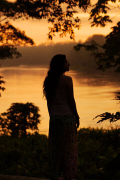 Silhouette of woman by river at tropical rainforest during sunrise
