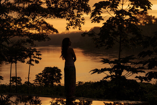 Silhouette of woman meditating in tropical rainforest at sunrise