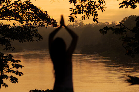 Silhouette of woman meditating in tropical rainforest at sunrise
