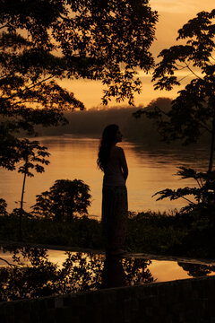 Silhouette of woman by river at tropical rainforest during sunrise