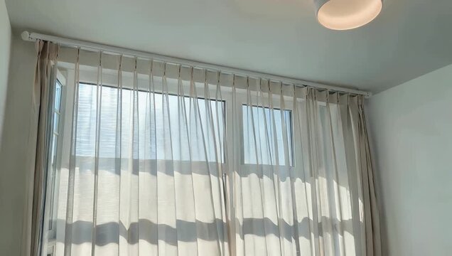 Atmospheric 4K Ultra HD high quality footage where sunshine and wind blows strongly through an open window into a room featuring the natural sun and shadows interacting through the sheer transparent