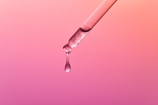 Close up of a Pipette Releasing Liquid on Gradient Pink Background.