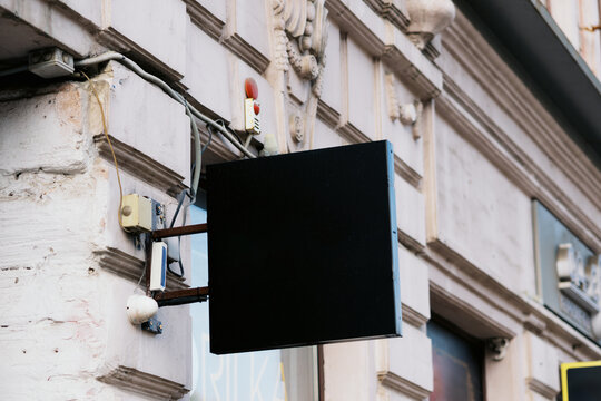 Empty Black Sign With Hooks on a Building Wall in a City