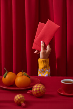 Close-up shot of a hand holding two red envelopes with oranges