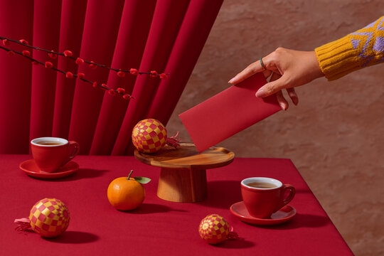 A festive still life of a hand with a red envelope with tea cups