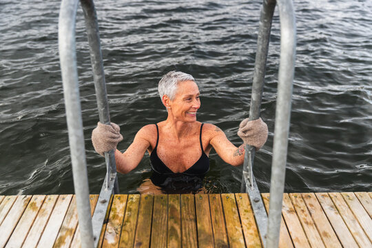 Happy Mature Woman Climbing Ladder from Cold Lake