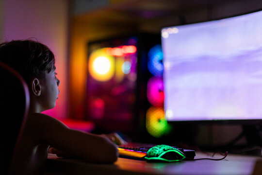 Child immersed in pc gaming, enjoying colorful lights 
