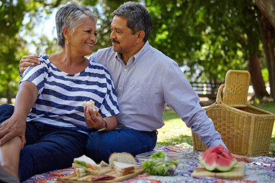 Picnic, sandwiches and senior couple relax at park for anniversary, healthy lunch and bonding. Retirement, food and old people with romantic date outdoor for marriage trust, love and support with hug - Powered by Adobe